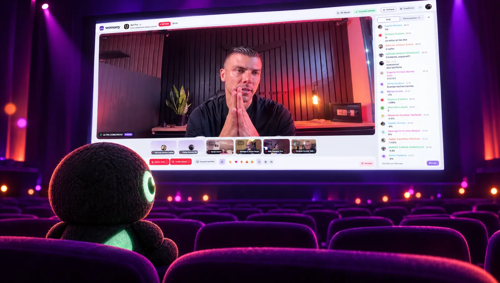 We sentado en la primera fila de un auditorio mira la pantalla gigante con una transmisión en vivo real de WEMANY: el anfitrión de ULTRA Comunidad, el chat y los participantes en la gradería
